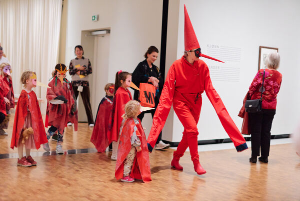 Opnar museet i knallraud dress, spiss hatt og nebb
